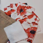 Lot de sept carrés démaquillants lavables au motif coquelicots rouges sur fond blanc, disposés en éventail à côté de leur pochon en lin beige Cocon Couture, un carré retourné montrant le côté éponge blanc.