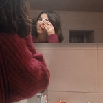 Femme se démaquillant le visage avec un carré démaquillant lavable Coquelicots devant son miroir de salle de bain.