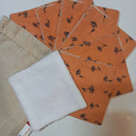 Lot de sept carrés démaquillants lavables au motif fleurs printanières orange, disposés en éventail sur fond blanc à côté de leur pochon en lin beige Cocon Couture, un carré retourné montrant le côté éponge blanc.
