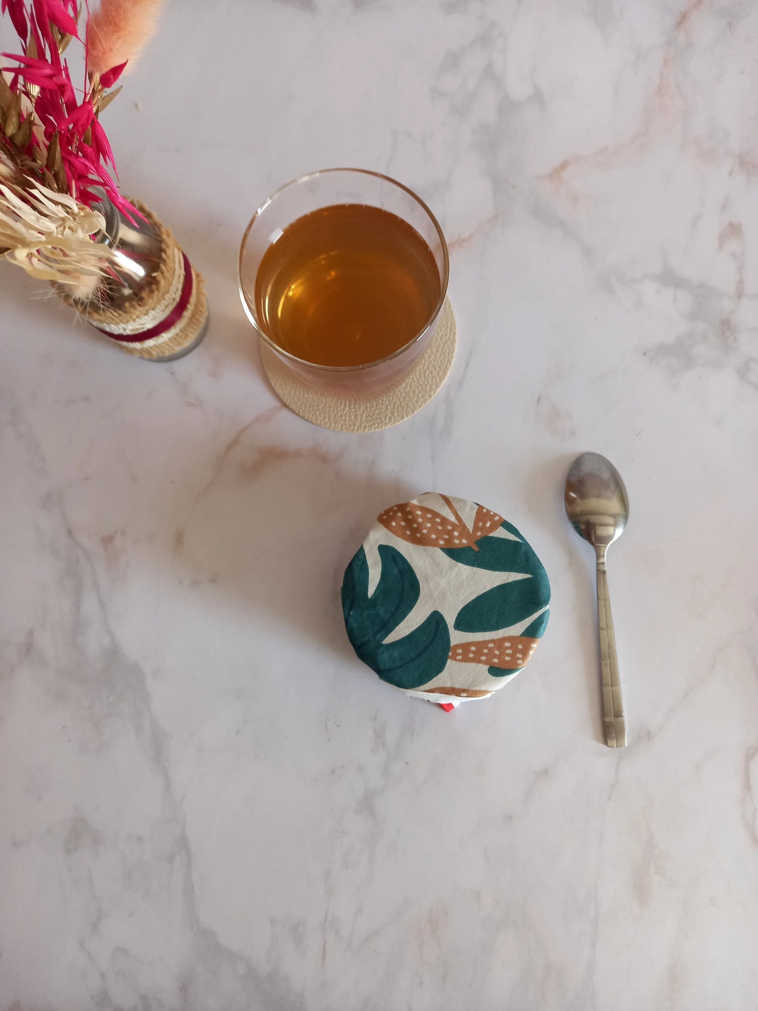 Charlotte alimentaire lavable à feuilles de palmier posée sur un petit ramequin, sur un plan de travail en marbre, près d'un verre de thé et d'une cuillère.