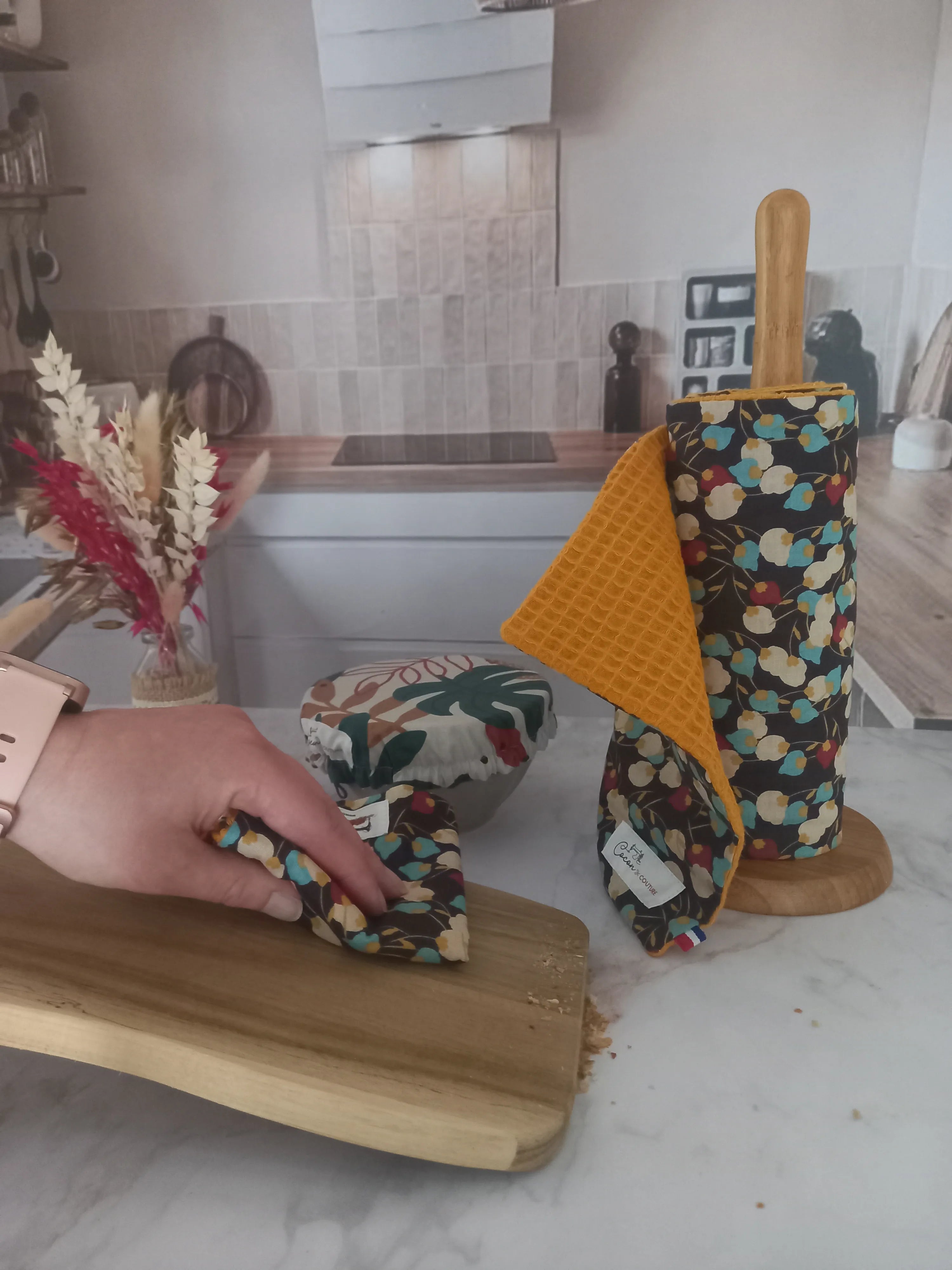 Dans une cuisine, sur un plan de travail en marbre, il y a de posé un rouleau d'essuie tout, une feuille d'essuie tout et une couvre bol sur un bol.