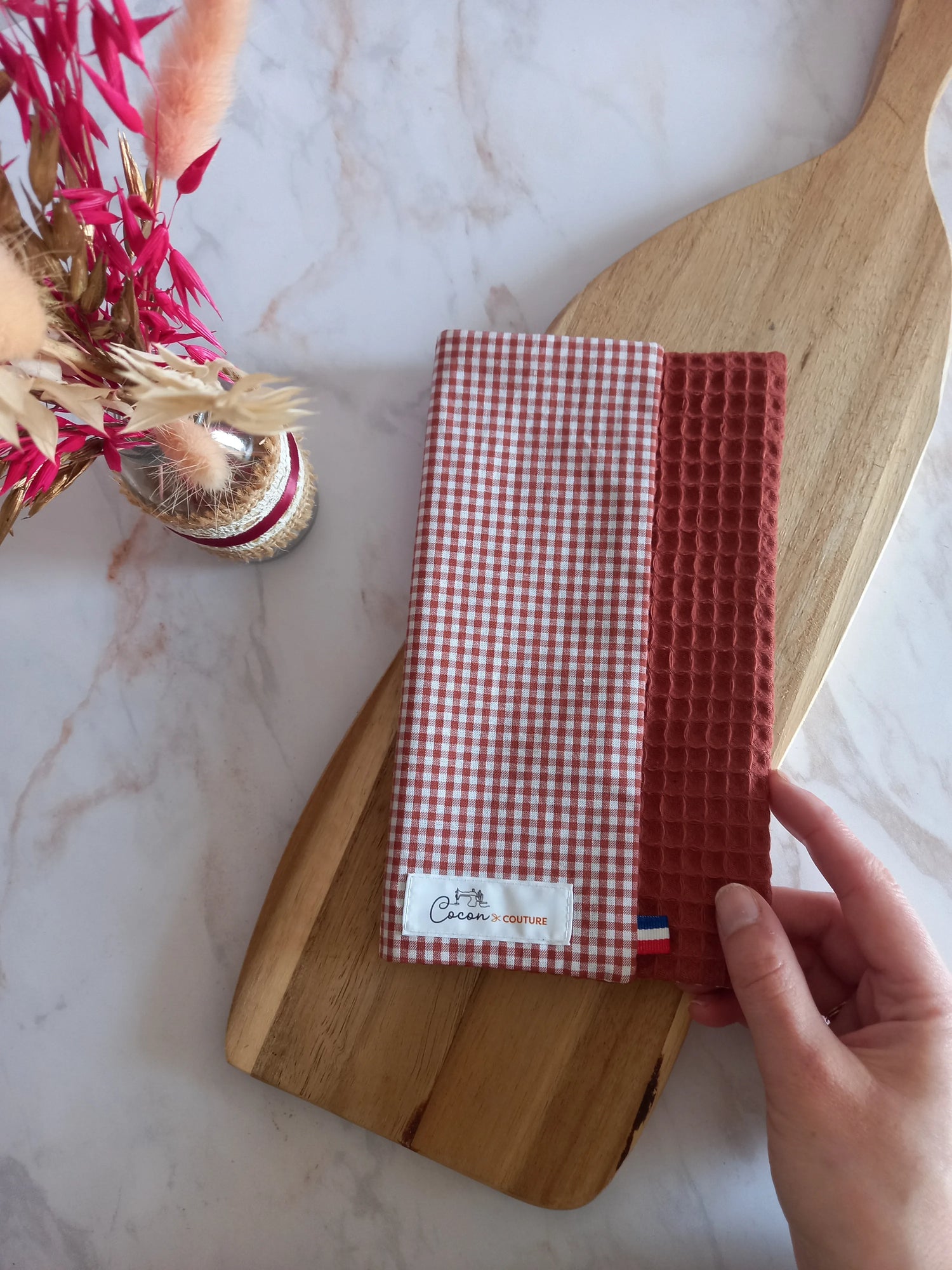 La feuille essuie-tout lavable est pliée sur une planche en bois. On aperçoit son recto à carreaux vichy terracotta, son envers en nid d'abeille terracotta et l'étiquette Cocon Couture.