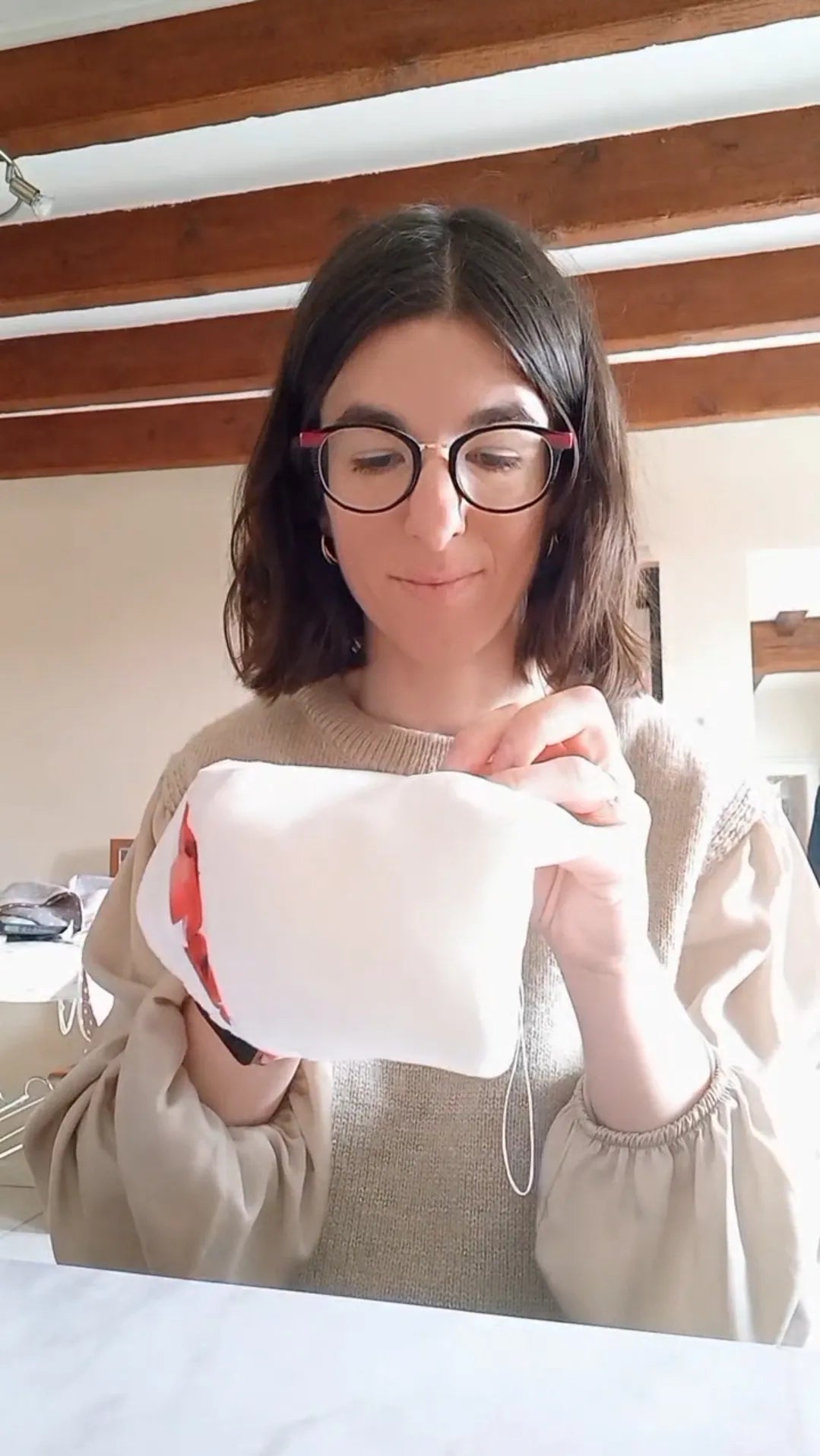Manon, la créatrice de Cocon Couture, tient une de ses créations en tissu éponge blanc à motif floral rouge.