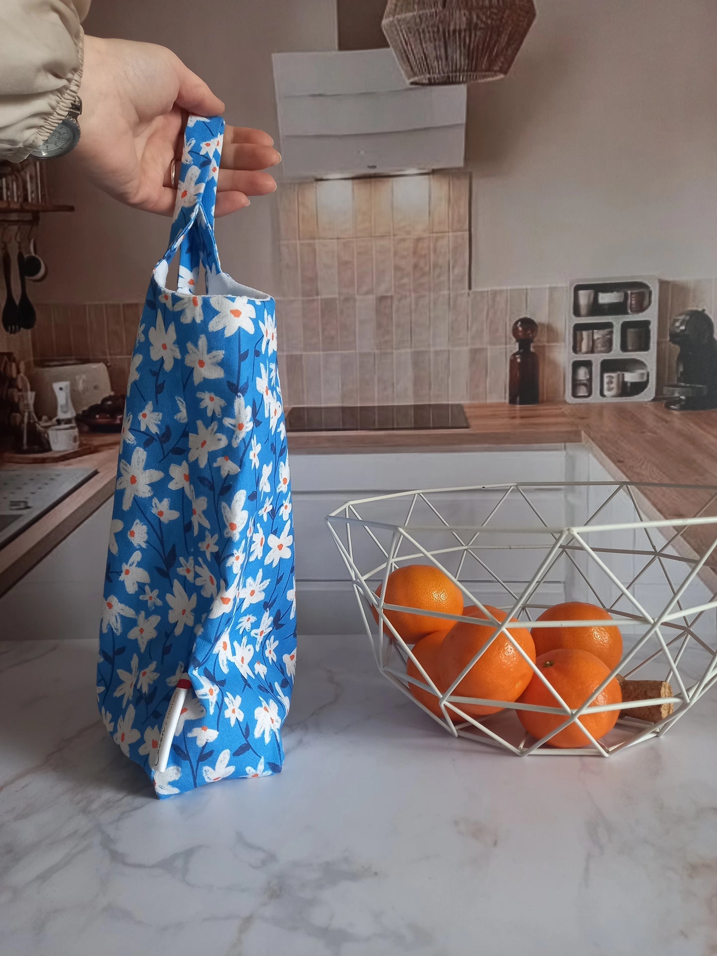 Main tenant un pochon alimentaire en coton motif fleuri bleu par son anse, vue de profil dans une cuisine