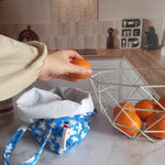 Pochon alimentaire en coton motif fleuri bleu avec l'étiquette Cocon Couture et une main y déposant une orange