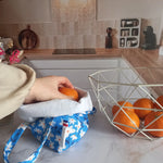 Pochon alimentaire en coton motif fleuri bleu avec étiquette Cocon Couture, une main y déposant une orange