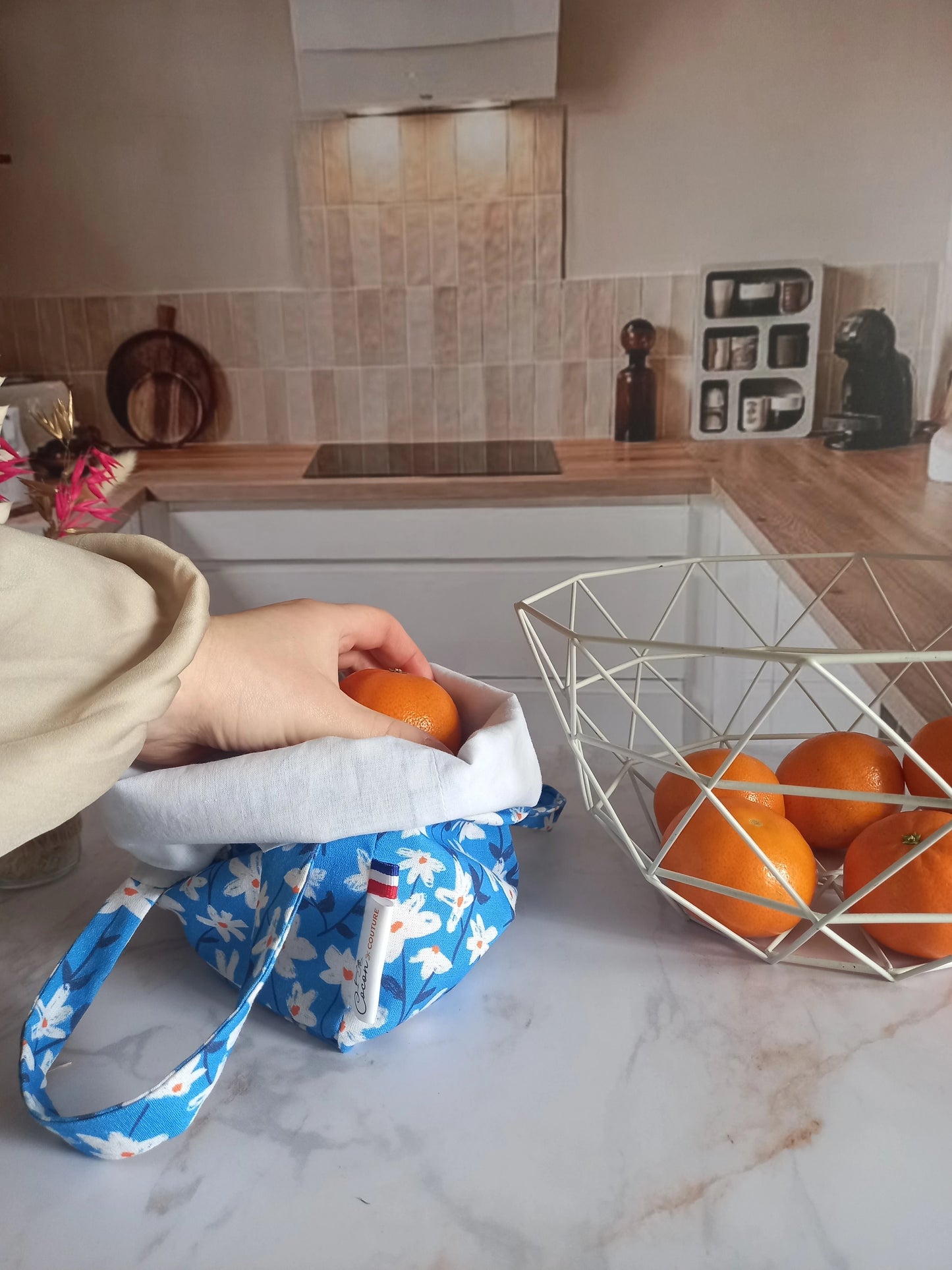 Pochon alimentaire en coton motif fleuri bleu avec étiquette Cocon Couture, une main y déposant une orange