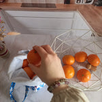 Main saisissant une orange au-dessus d'un pochon alimentaire motif fleuri bleu, vue de dessus