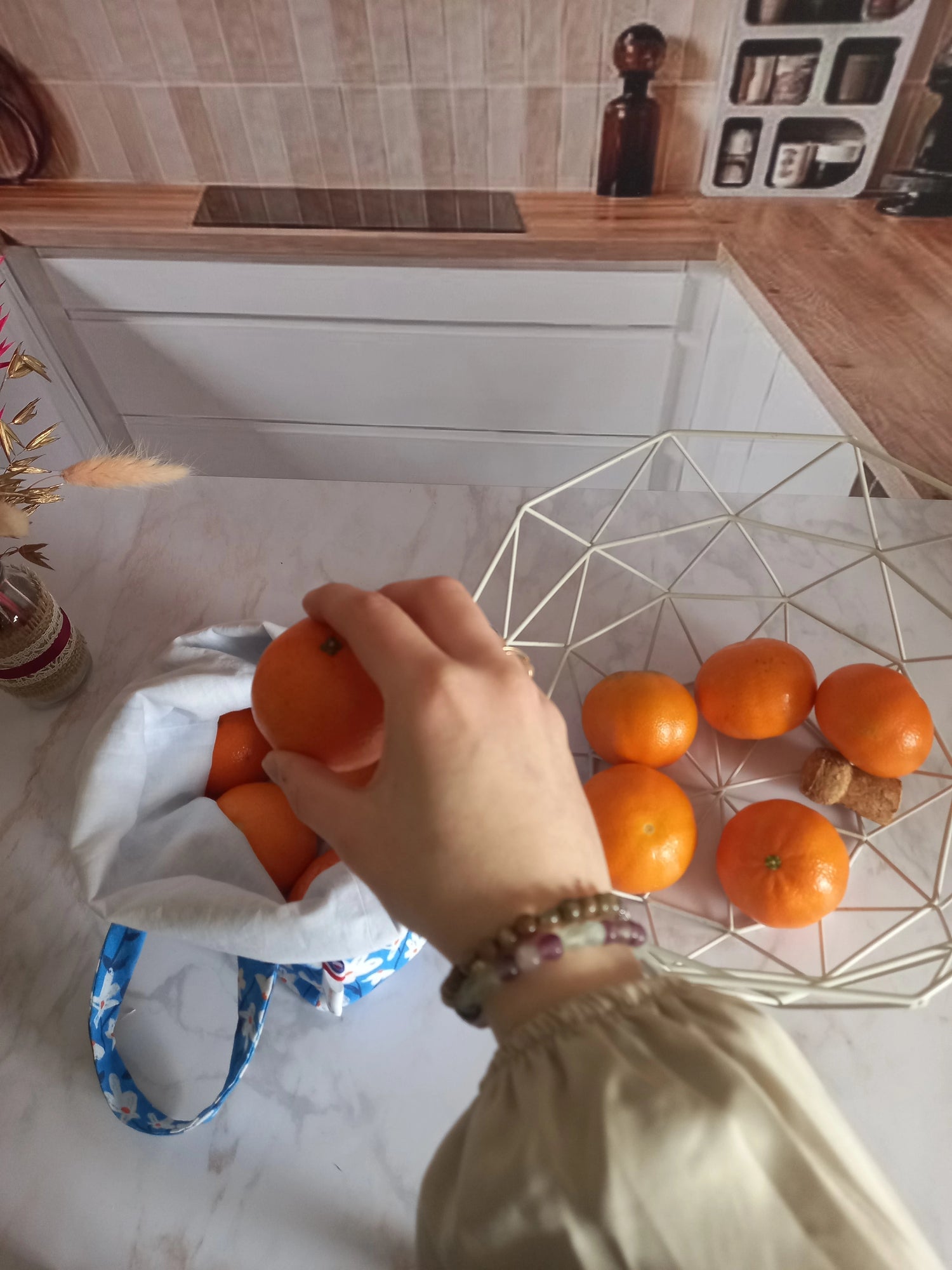 Main saisissant une orange au-dessus d'un pochon alimentaire motif fleuri bleu, vue de dessus