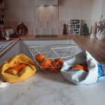 Deux pochons alimentaires Cocon Couture avec des oranges sur un plan de travail de cuisine, collection Soleil et collection fleurs