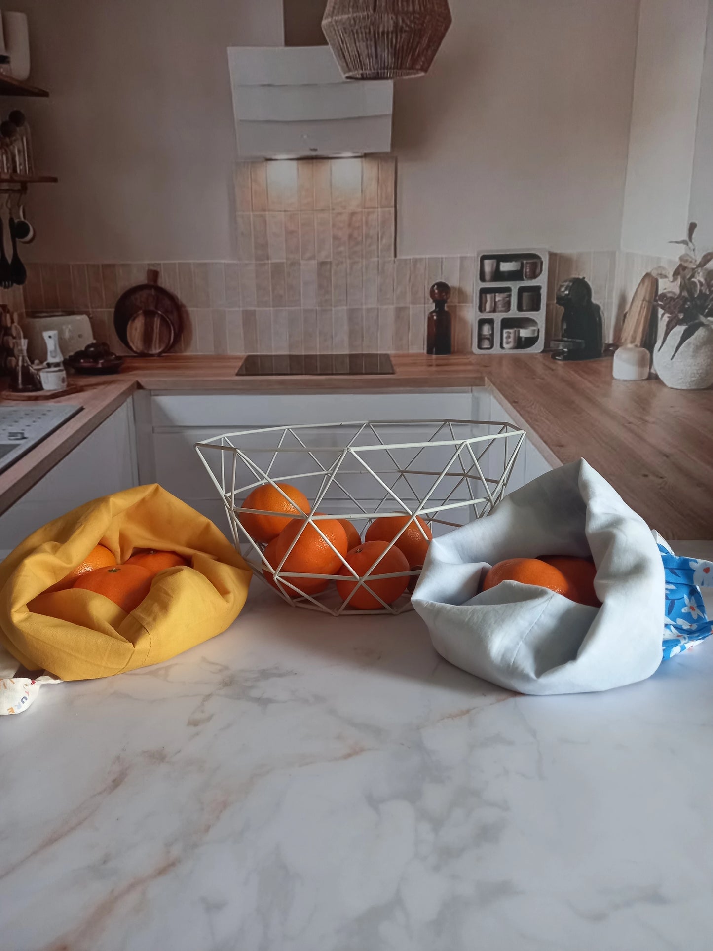 Deux pochons alimentaires Cocon Couture avec des oranges sur un plan de travail de cuisine, collection Soleil et collection fleurs
