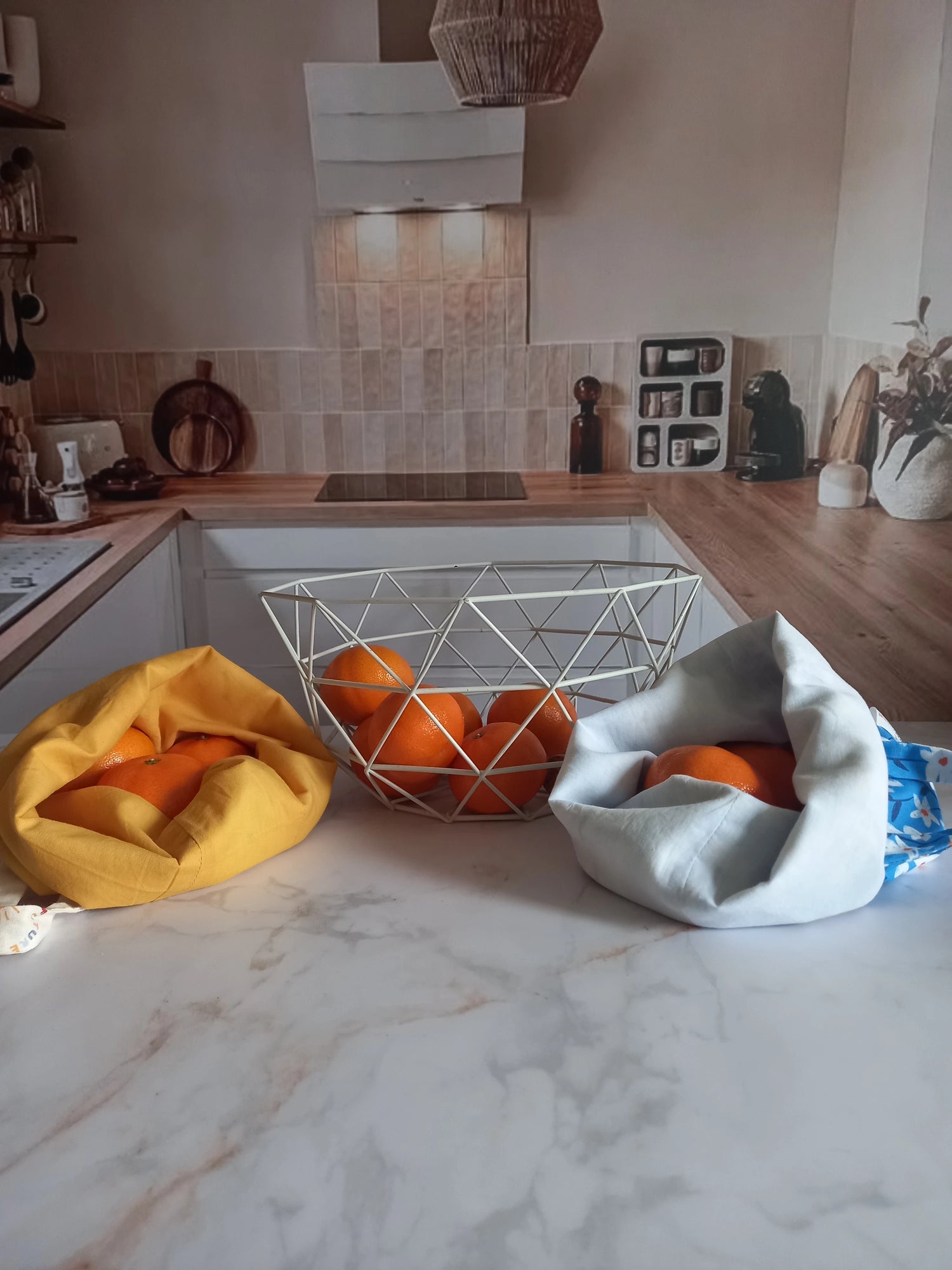 Deux pochons alimentaires Cocon Couture avec des oranges sur un plan de travail de cuisine, collection Soleil et collection fleurs