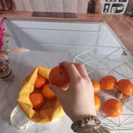 Vue de dessus d'une main tenant une orange au-dessus d'un pochon alimentaire collection Soleil rempli d'oranges