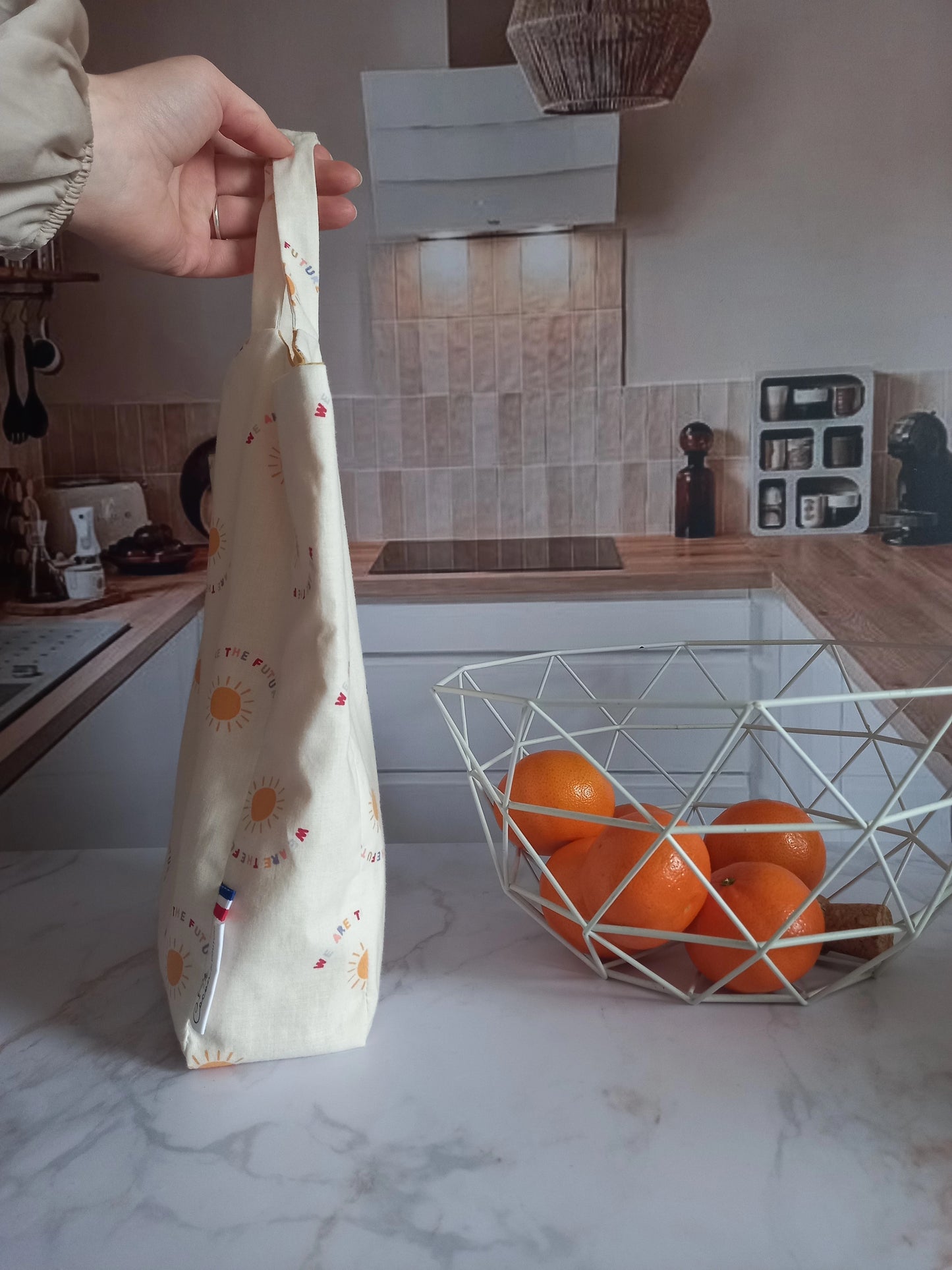 Main tenant un pochon alimentaire collection Soleil par ses anses dans une cuisine