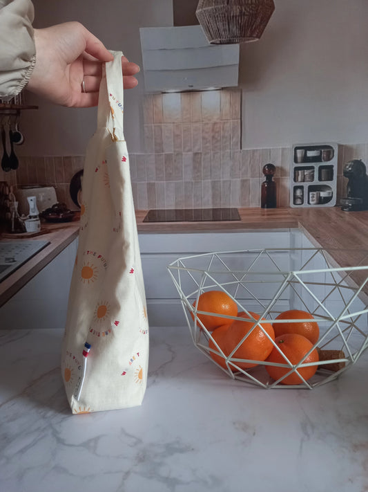Main tenant un pochon alimentaire collection Soleil par ses anses dans une cuisine