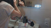 Une femme se démaquille le visage avec un carré démaquillant lavable devant son miroir, puis une feuille essuie-tout lavable sert à nettoyer une planche en bois couverte de miettes de pain dans la cuisine