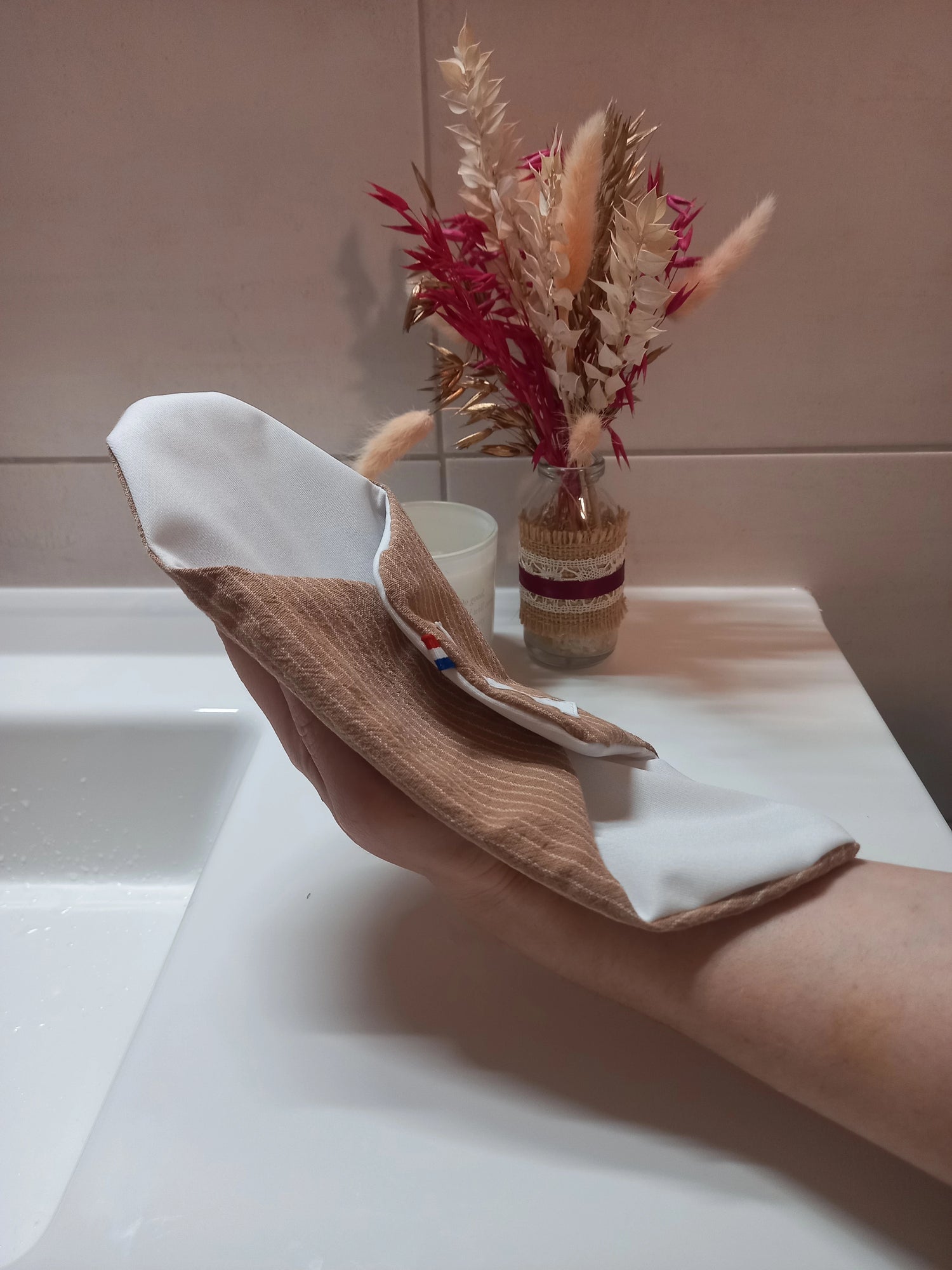 Le protège-slip en coton lavable est posé sur une main, montrant son côté coton rayé beige et son côté en tissu imperméable blanc, avec un ruban tricolore.