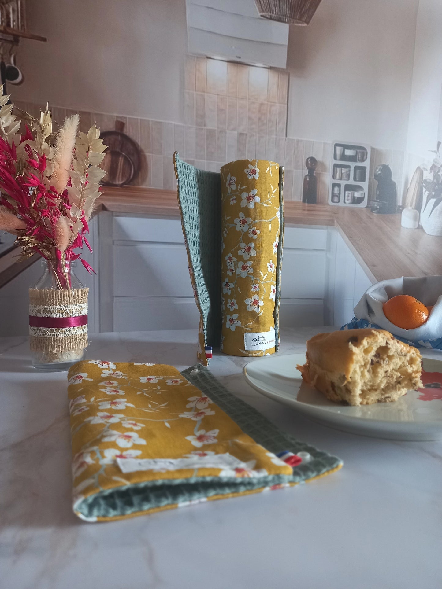 Rouleau essuie-tout lavable Cerisier ouvert et roulé dans une cuisine avec, à côté, des fleurs séchées et un gâteau