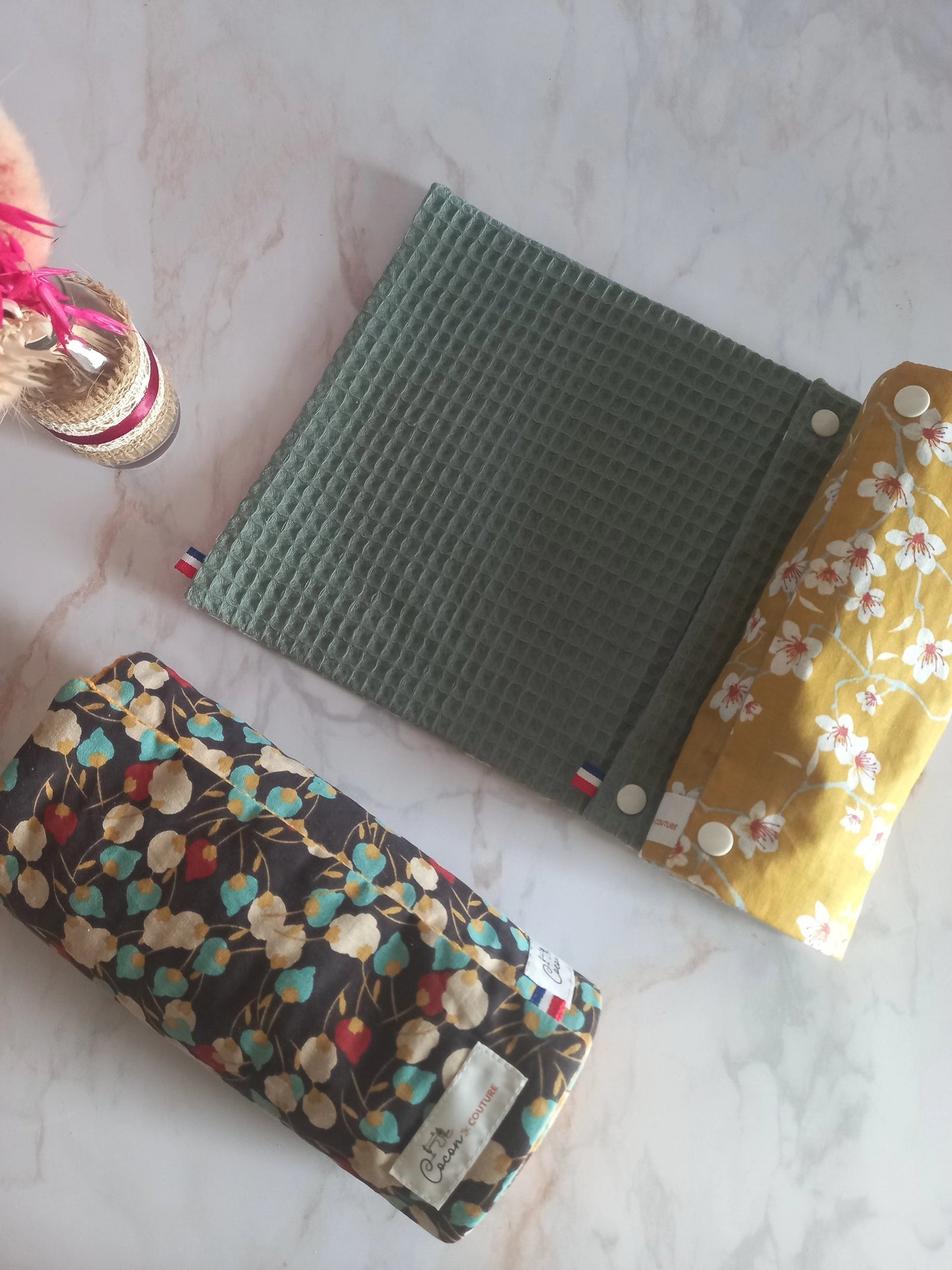 Deux rouleaux d'essuie-tout lavables Cocon Couture dont un de la collection Cerisier et l'autre de la collection Muguet, posés sur un plan de travail avec, à côté, des fleurs séchées