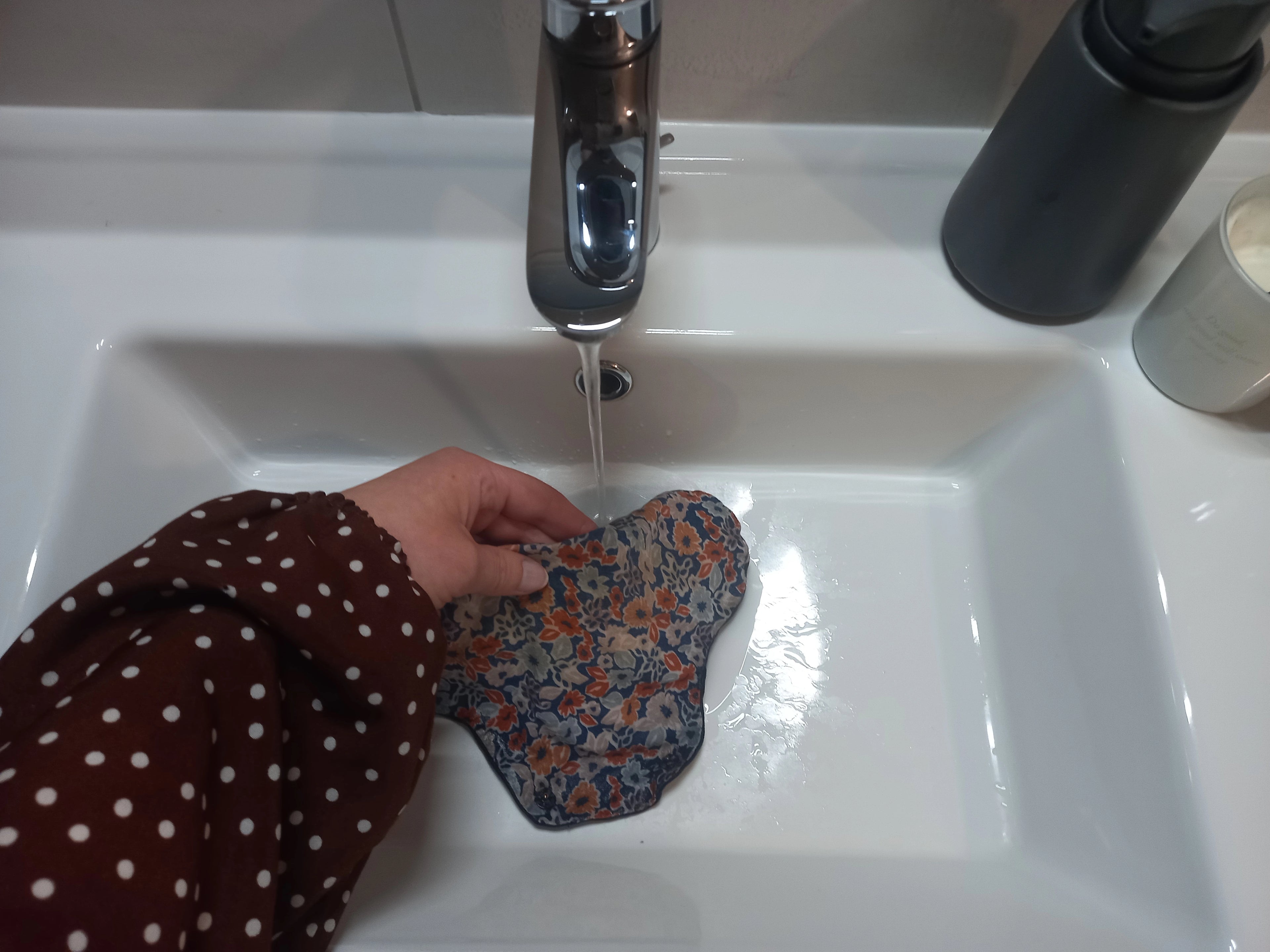 Une serviette menstruelle est rincée sous l'eau dans une salle de bain.