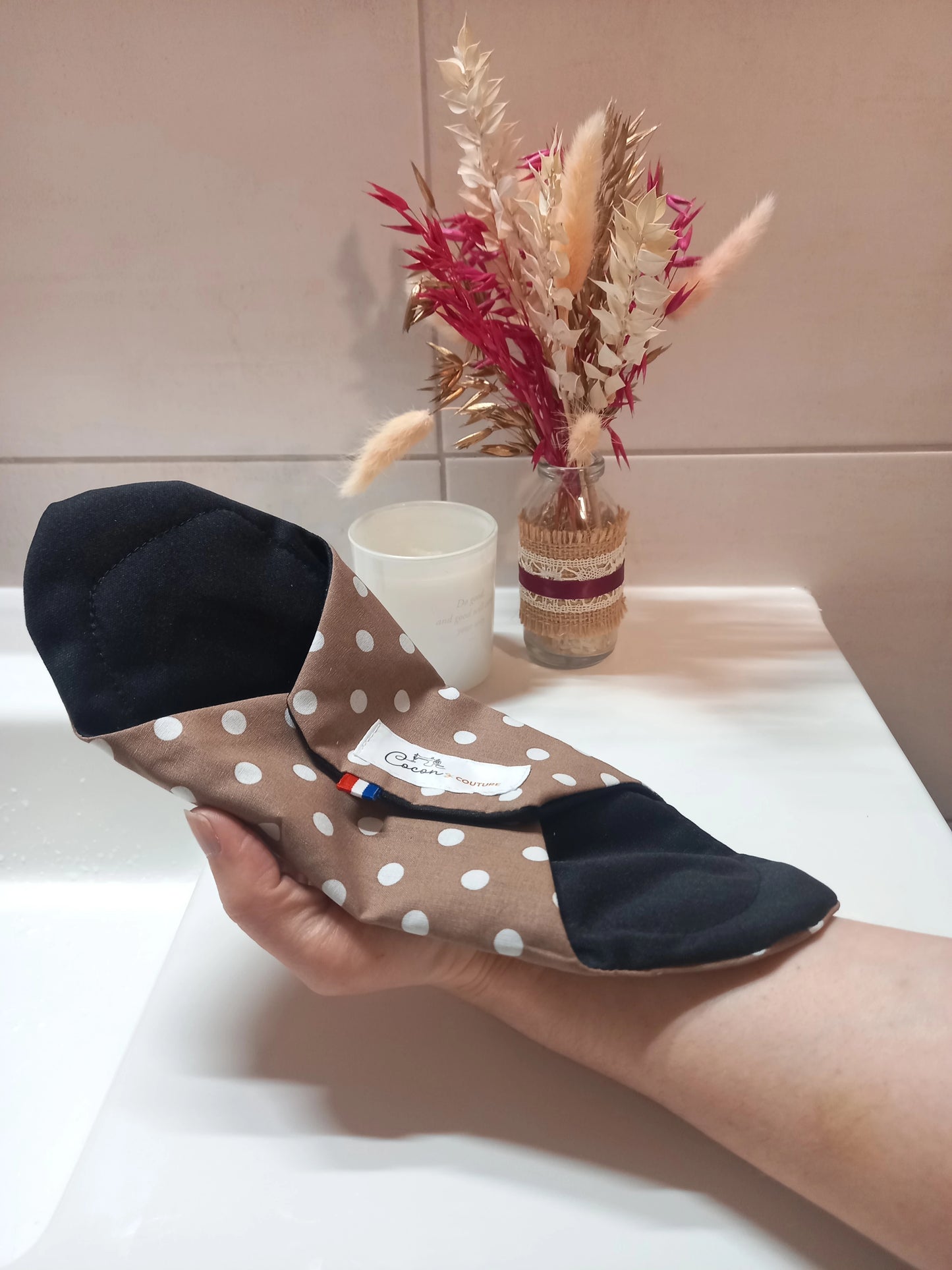 La serviette menstruelle lavable à pois est tenue dans une main. Le côté lingerie en tissu imperméable bleu marine est visible, ainsi que les ailes latérales.