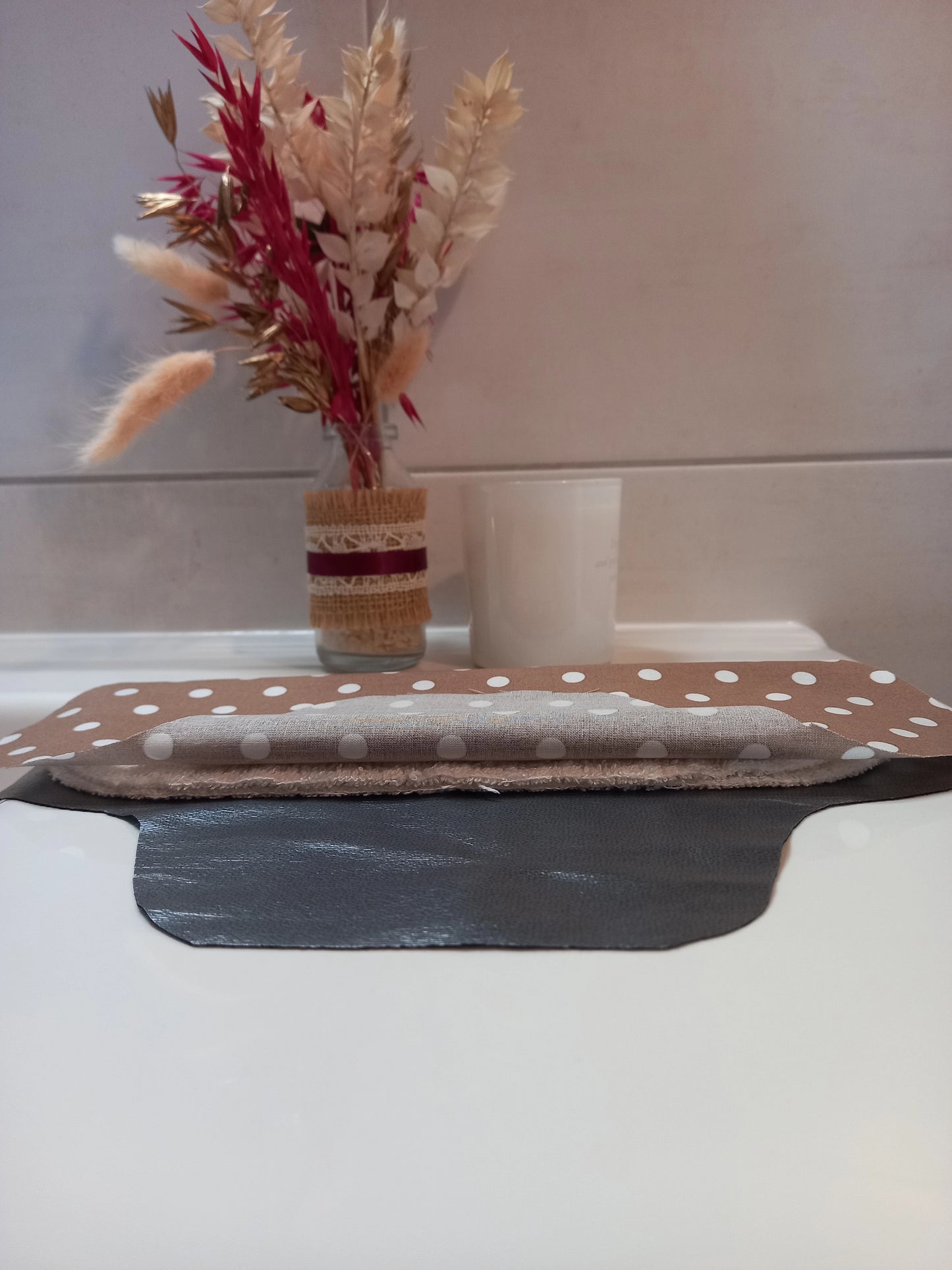 La serviette menstruelle lavable à pois est présentée en coupe, non cousue. On distingue le côté motif en coton, les deux épaisseurs de tissu éponge absorbant et la face imperméable grise.