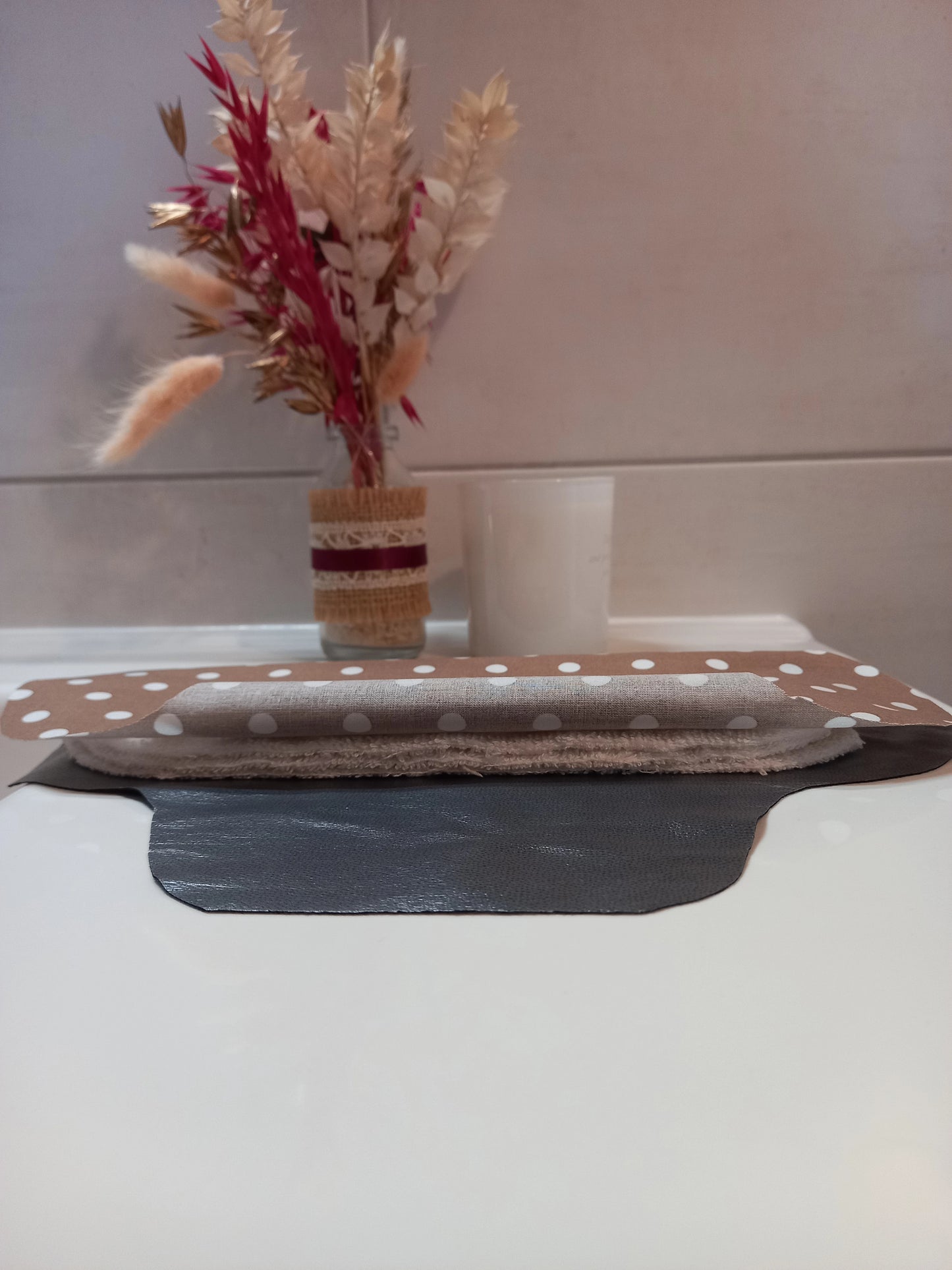 La serviette menstruelle lavable à pois est présentée en coupe, non cousue, pour montrer sa composition. On distingue le côté motif en coton, les trois épaisseurs de tissu éponge absorbant et la face imperméable grise.